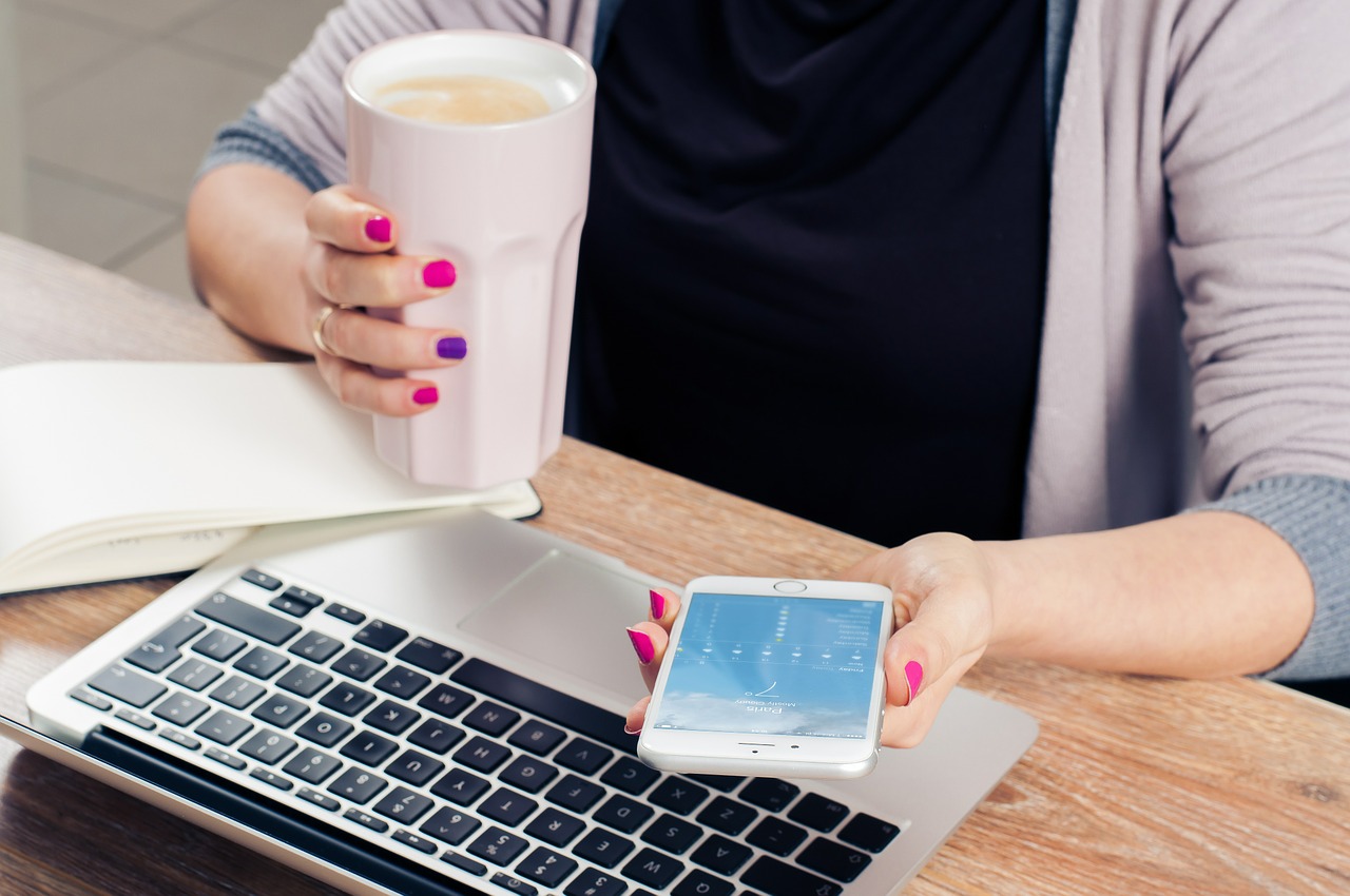 Womans Hand holding a mobile phone while the other is holding a glass